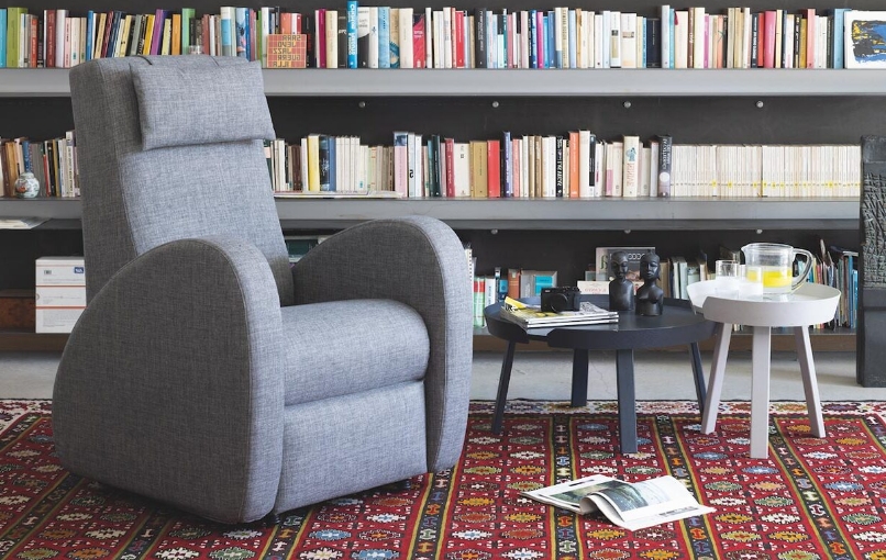 Aufstehsessel Zoe in grauem Stoff vor einer Bücherwand